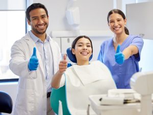 Two dentists and a patient giving a thumbs up.